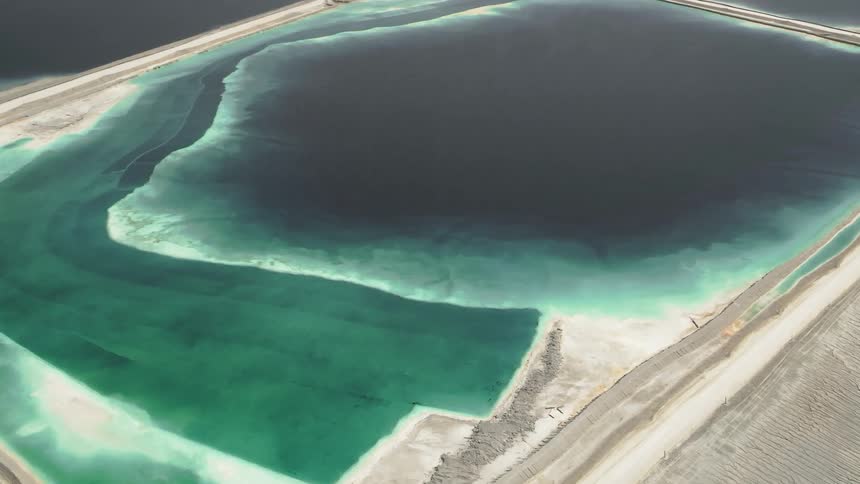 A large industrial pond sits amongst white soil at a chemical plant