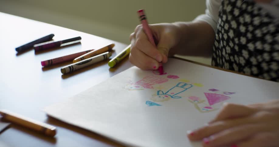 A young child draws a picture of her family with crayons