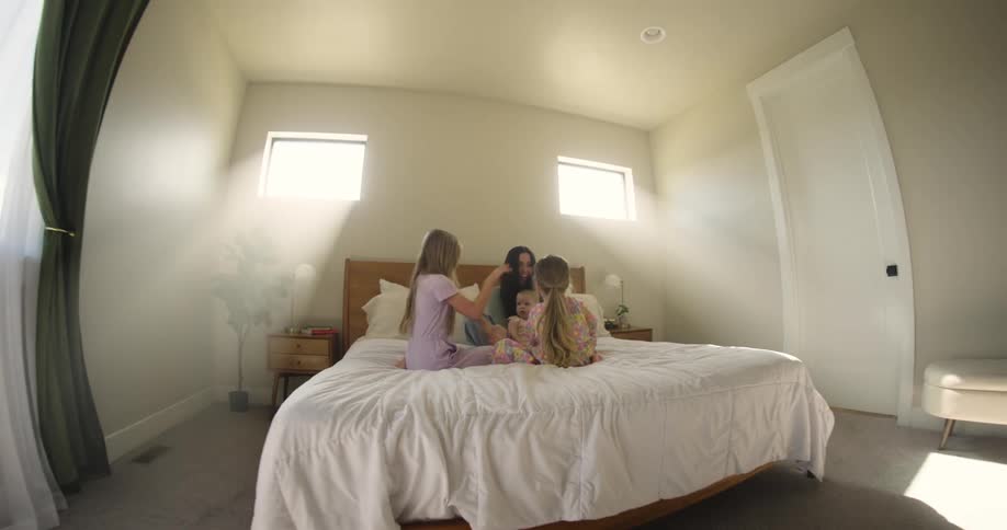 Mother sitting on bed with baby and two small children playing
