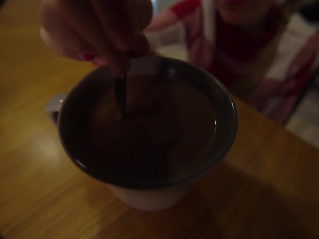 Person in a chair reaches up to stir a mug of hot chocolate
