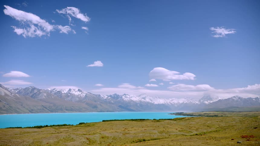 Landscape on a blue sky day with few clouds and a lake surrounded by snowy mountains