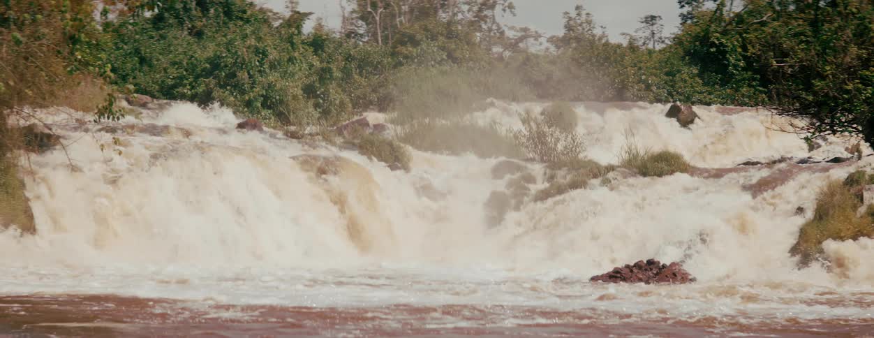 A small waterfall with lots of white foam and close to some green trees that are in the water