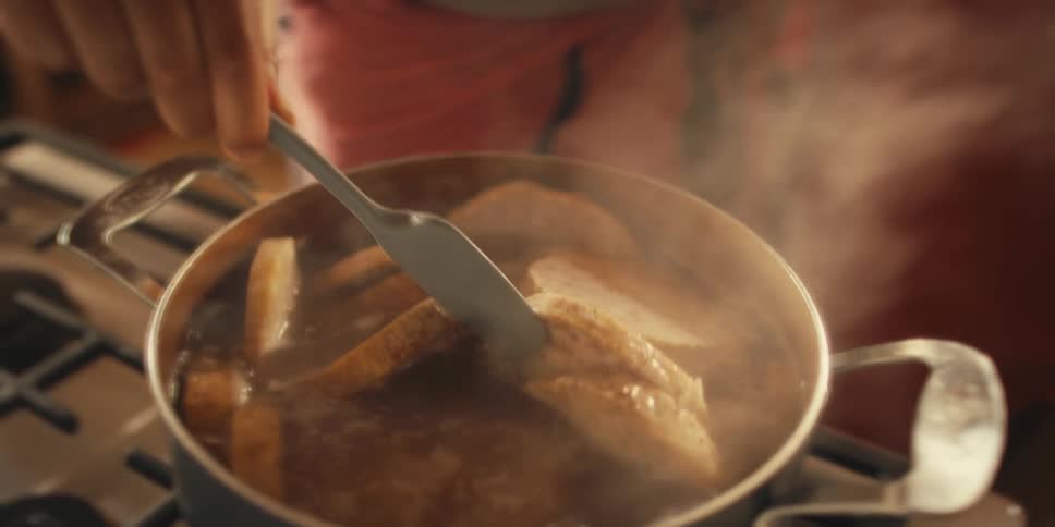 A person cooks food in a pot with steaming water