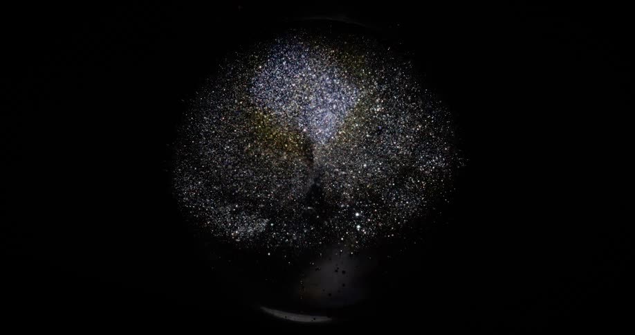 White and metallic particles float in a transparent globeagainst a black background