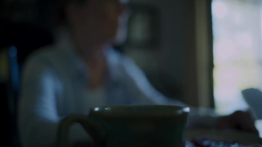 Close up of a cup evaporating smoke in the foreground and a woman eating in the background