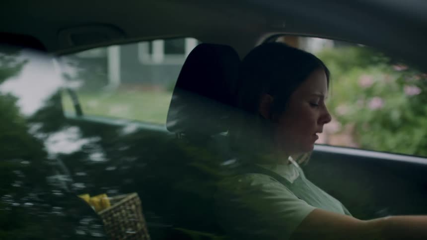 A woman puts a box of utilities in the back seat of car and then proceeds to sit on the driver seat
