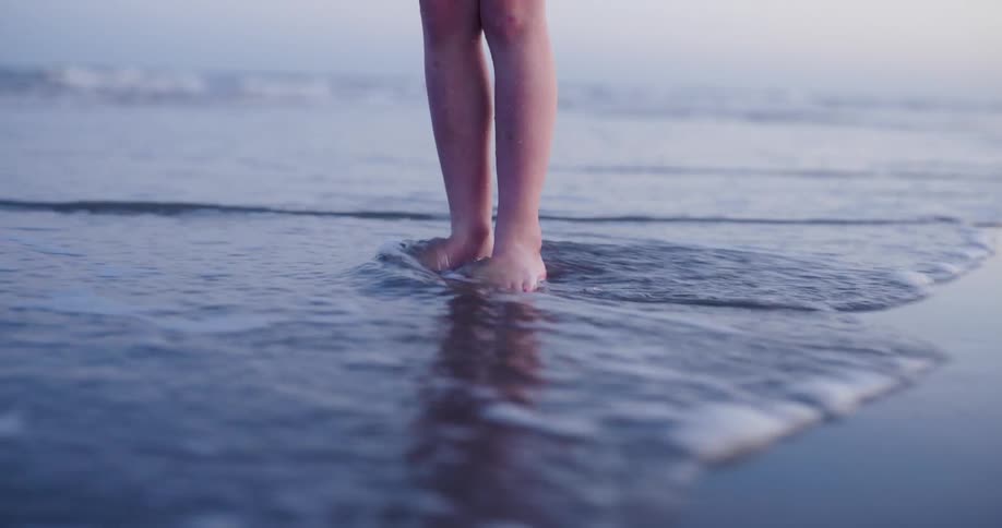 A young child stands on a beach as the tide comes in