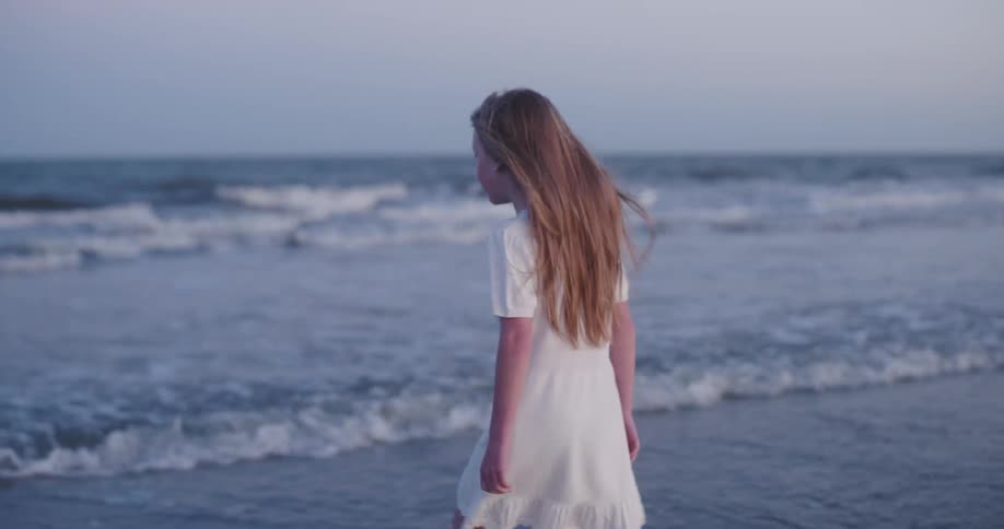 Girl in a white dress walking along the sea beach