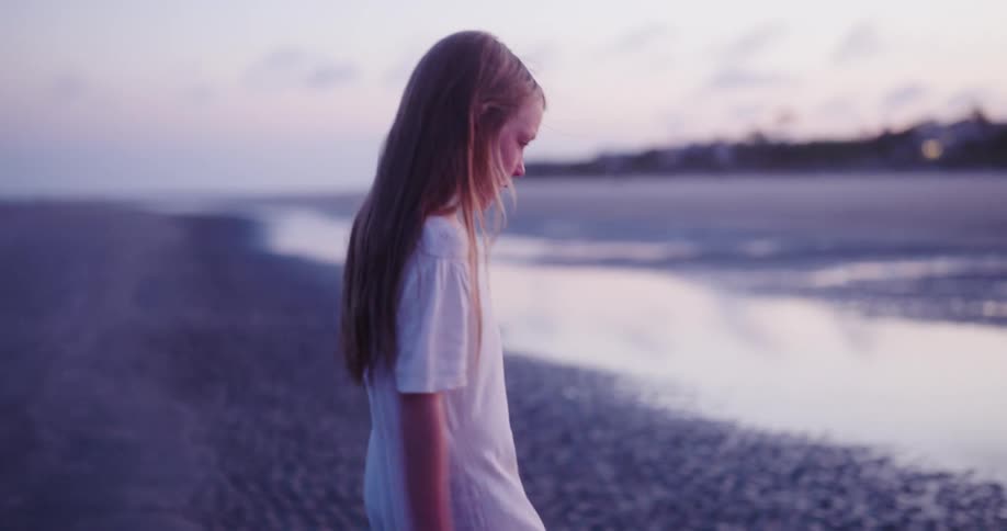 Blonde girl in white dress walking on the beach sand in a puddle of water