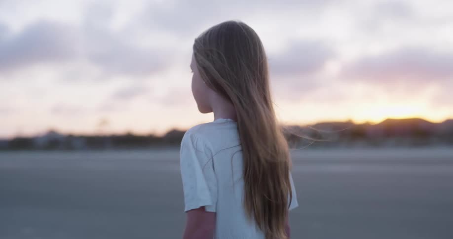 A young girl walks alone on the beach at sunset