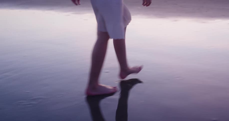 A young girl walks alone on the beach at sunset