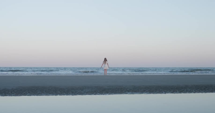 Girl walking on the beach with her feet in the water as waves roll into shore