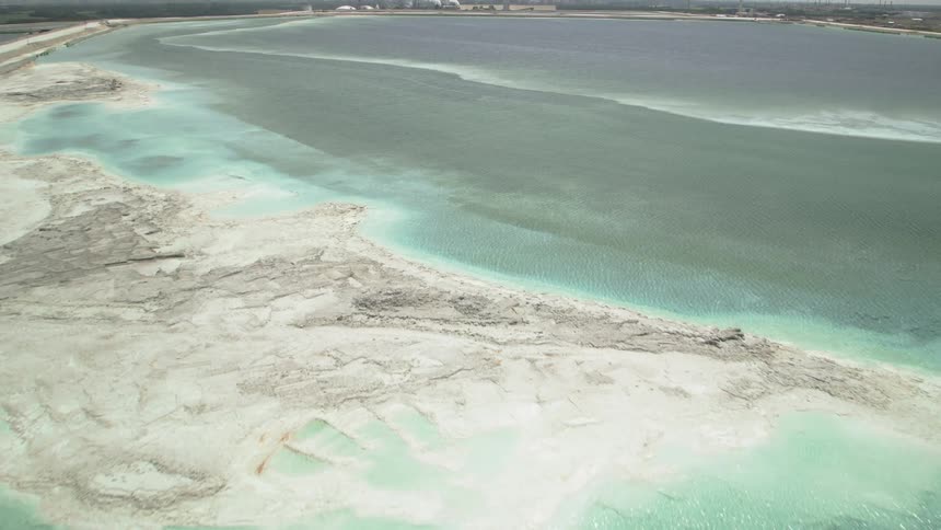 Aerial view of a turquoise waste pond surrounded by white sands