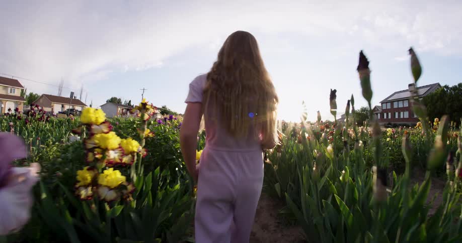 A young blonde girl walks through a field of flowers in a suburb