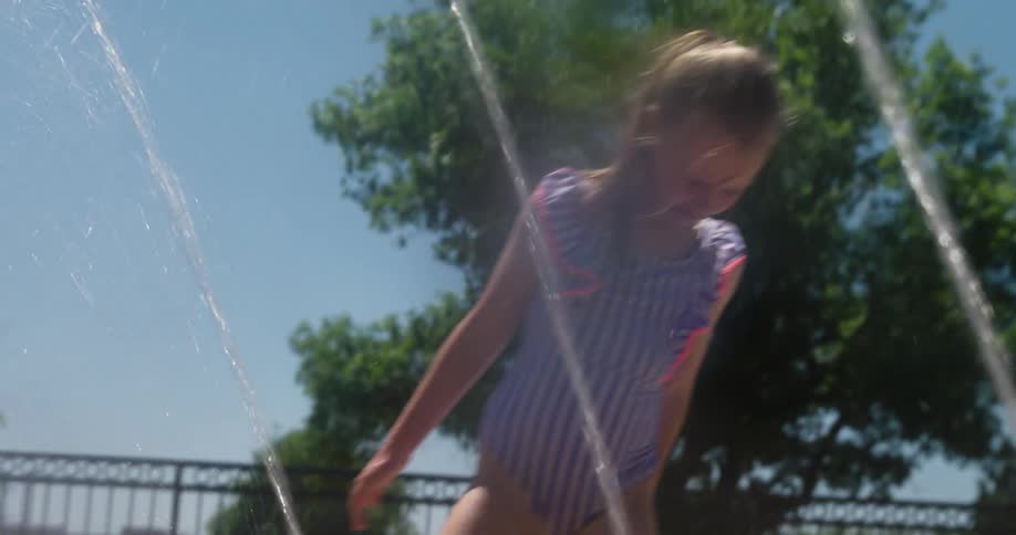 A little girl in a bathing suit is playing with jets of water coming out of the ground