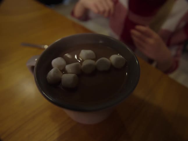 A child putting marshmallows in hot chocolate in a mug and then drinking it