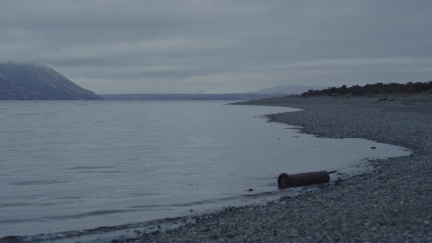 Lake with calm waters with mountains on the horizon on a cloudy day