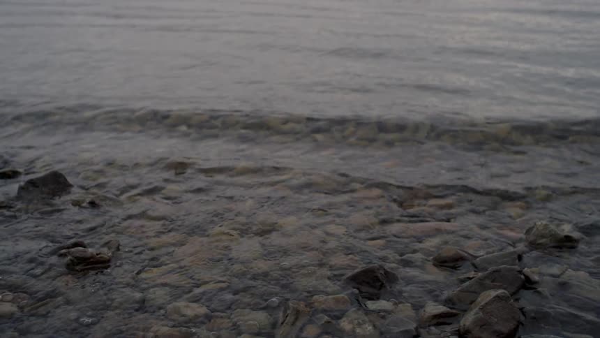 Waves roll into shore and over rocks and stones along the coast