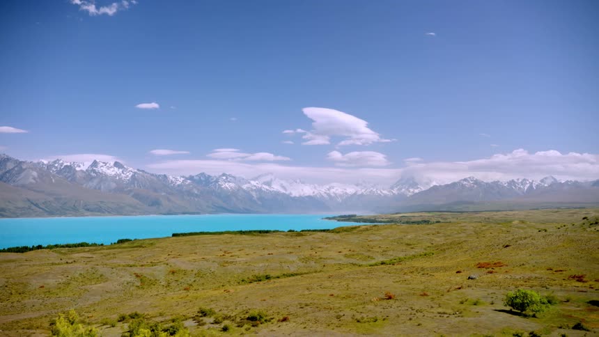 Stunning landscape with a turquoise lake grassy plains and snowcapped mountains under a clear blue sky
