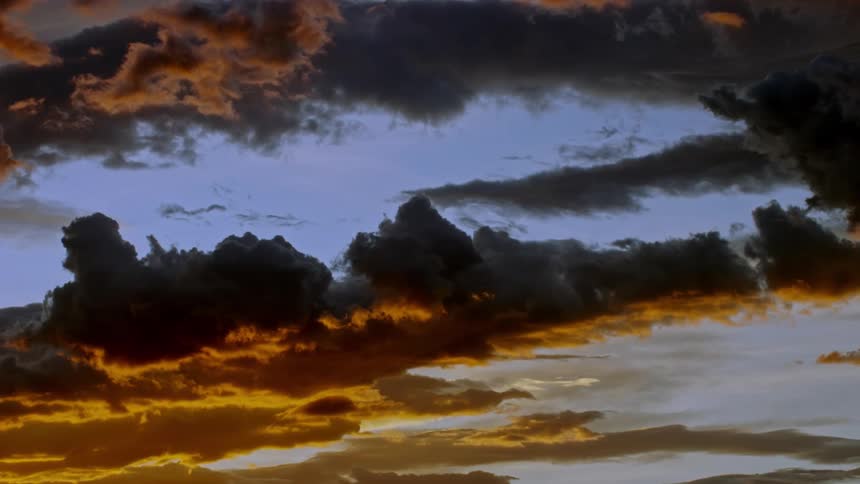 A dramatic sky filled with dark clouds and vibrant orange hues at sunset
