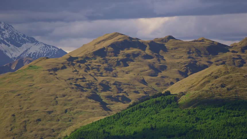 Greenish mountain range and a snowy mountain in the background with a cloudy sky