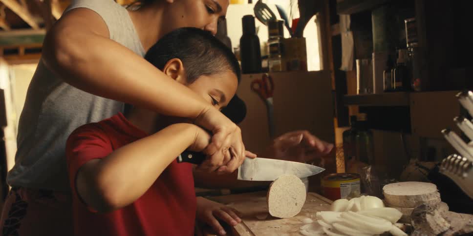 Mother and son together with a knife cutting a slice on top of a wooden board