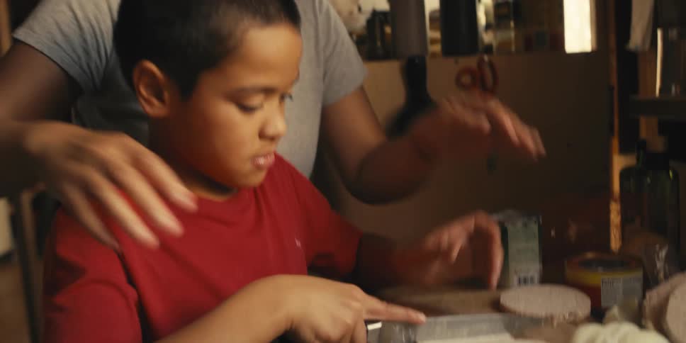 Mother guides son as the boy cuts a disk into wedges on the counter