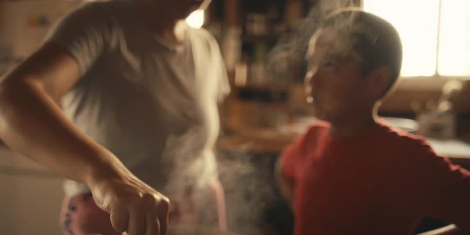 A mother is stirring food at the stove with her son