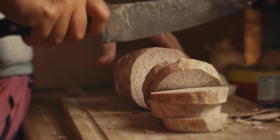 A woman slices up a taro root on a kitchen cutting board