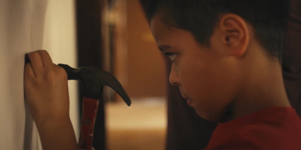 Concentrated boy hammering a nail into a wall