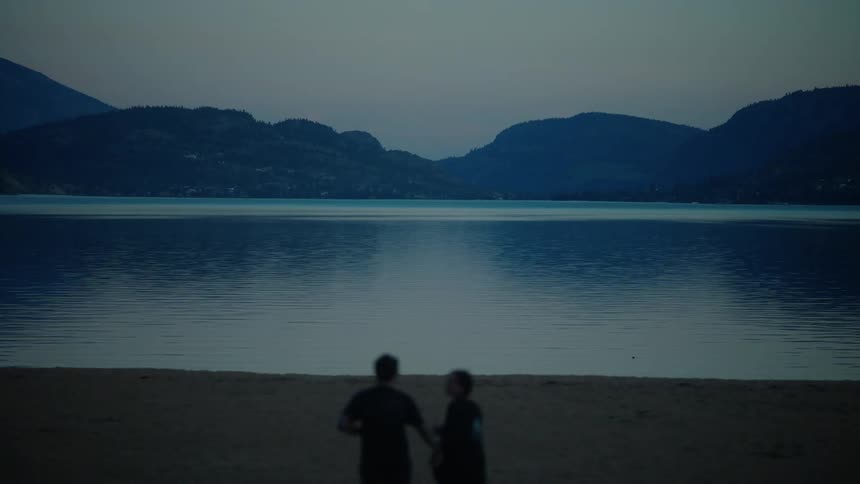 A man holds a womans hand as they run to a lake