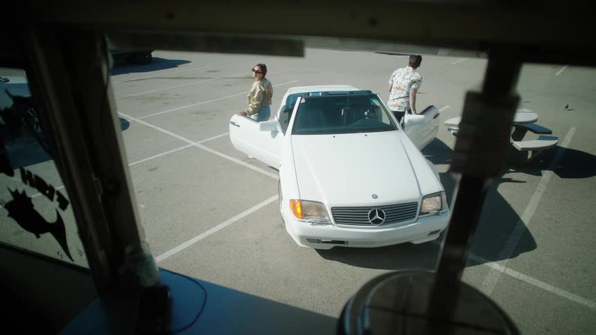 White vehicle with a man and a woman parked in front of a store with both getting out of the car