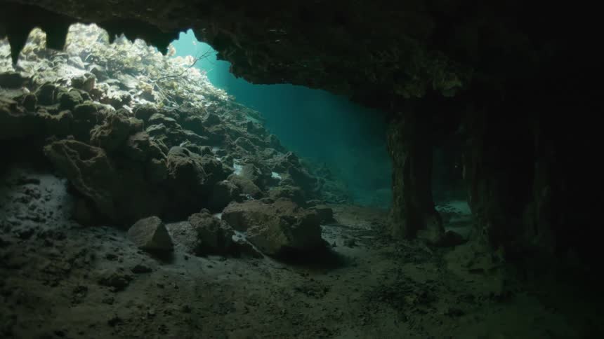 A sunlit underwater cave with rocky formations and clear blue water