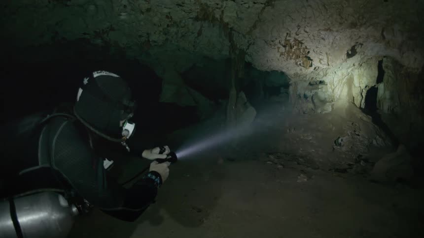 Scuba diver turns on a flashlight and aims it at a small underwater cave