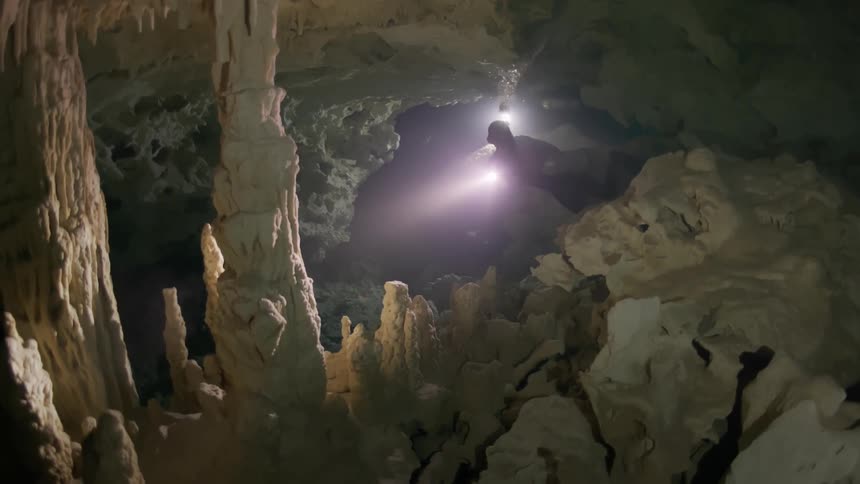 A person is exploring an underwater cave filled with stalagmites