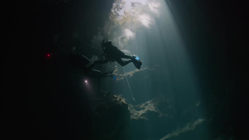 Divers exploring an underwater cave illuminated by sunlight filtering through the water