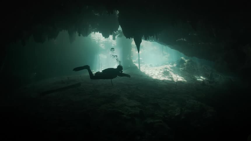 Silhouette of a diver swimming in an aquatic cave