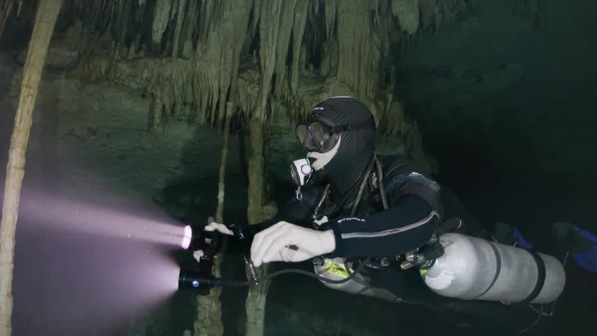 Person with cylinders diving in a cave submerged in water