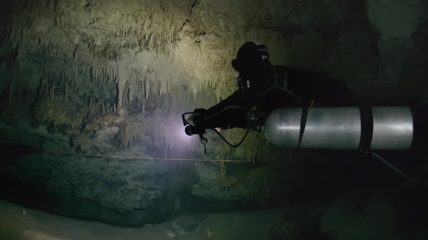 Diver with oxygen cylinders venturing into caves submerged in water
