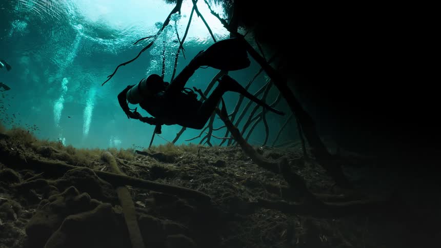 Scuba divers explore a small lake leading to flooded caverns
