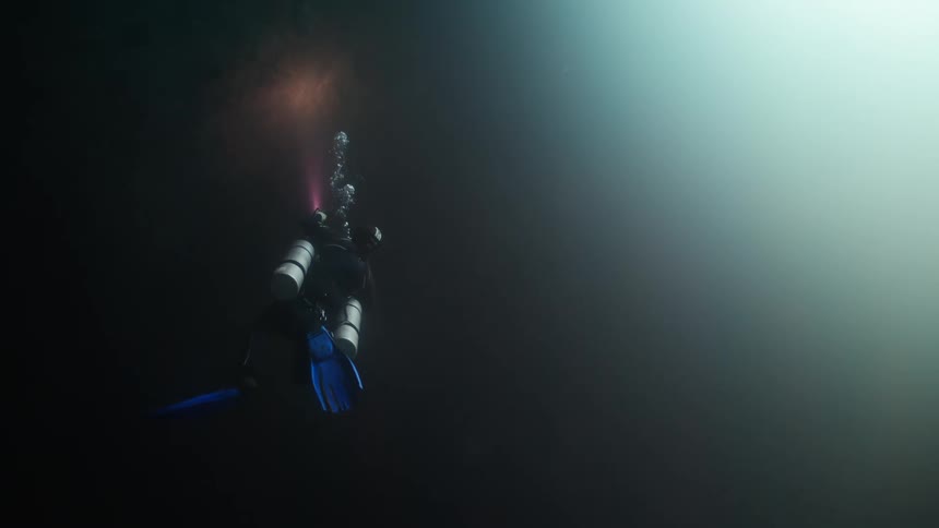 Portion of underwater cavern remains in shadow despite bright lit area and diver uses flashlight to illuminate stone surface in the shadows