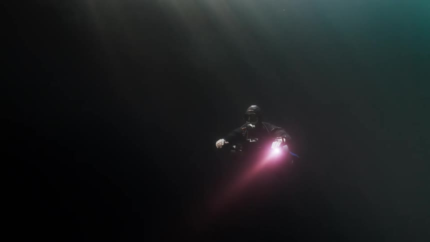 Diver venturing into an empty ocean underwater using an oxygen cylinder and a red light flashlight