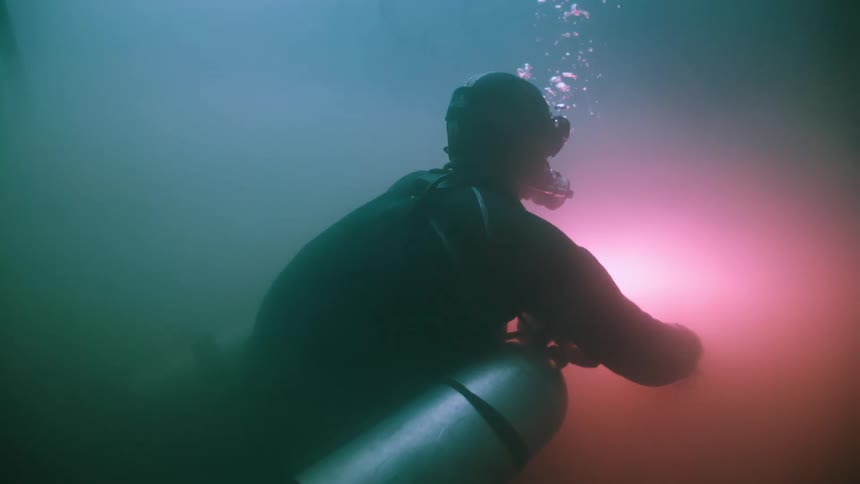 A scuba diver exploring underwater with a flashlight illuminating the murky water