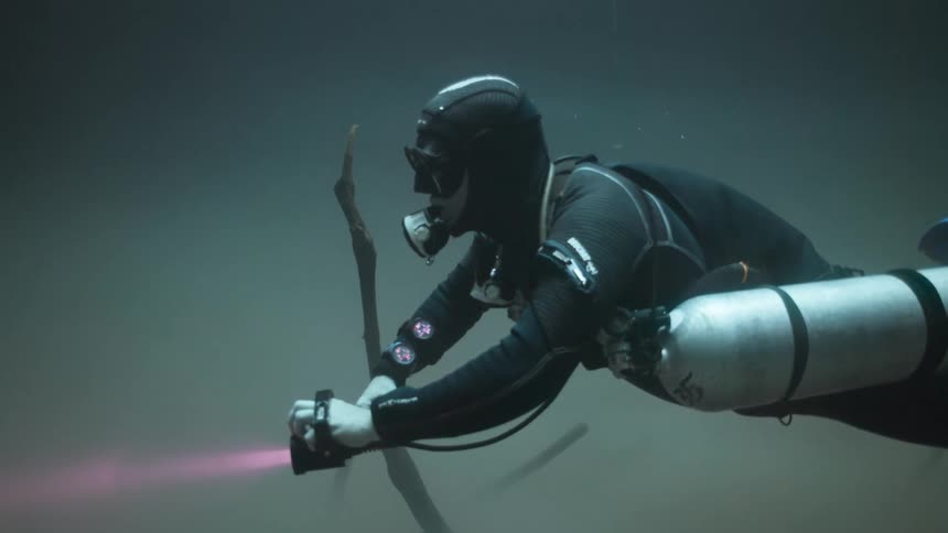 Person scuba diving with a red flashlight at the bottom of the ocean