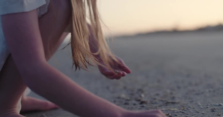 Pair of childs hands picking up shells in the sand on the beach