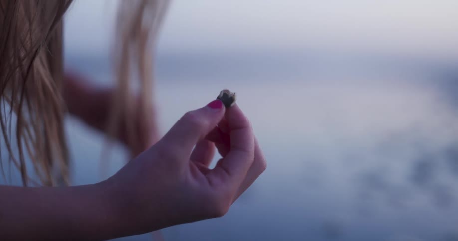A young girl holds a tiny hermit crab next to the ocean