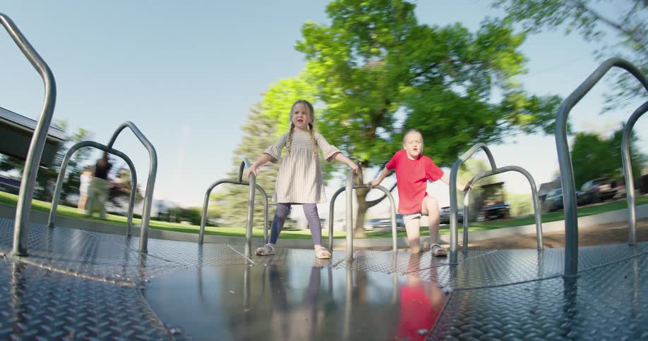 Little blonde girls leaning on a spinning ride in a park
