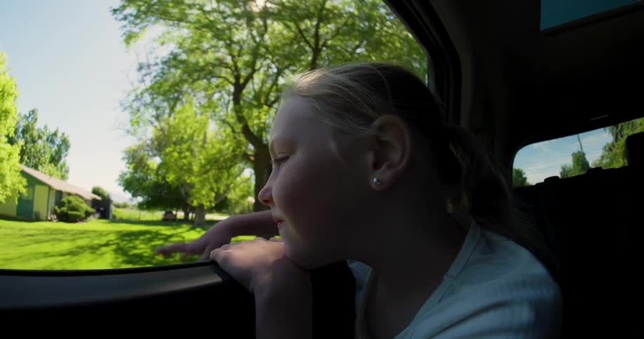 Portrait of a little blonde girl enjoying and catching a breeze in the window of a moving car
