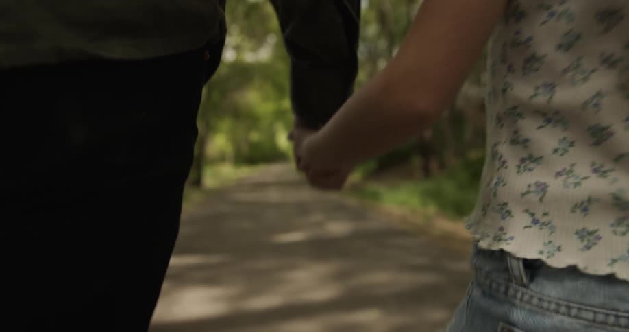Father and young daughter hold hands and walk a path with trees