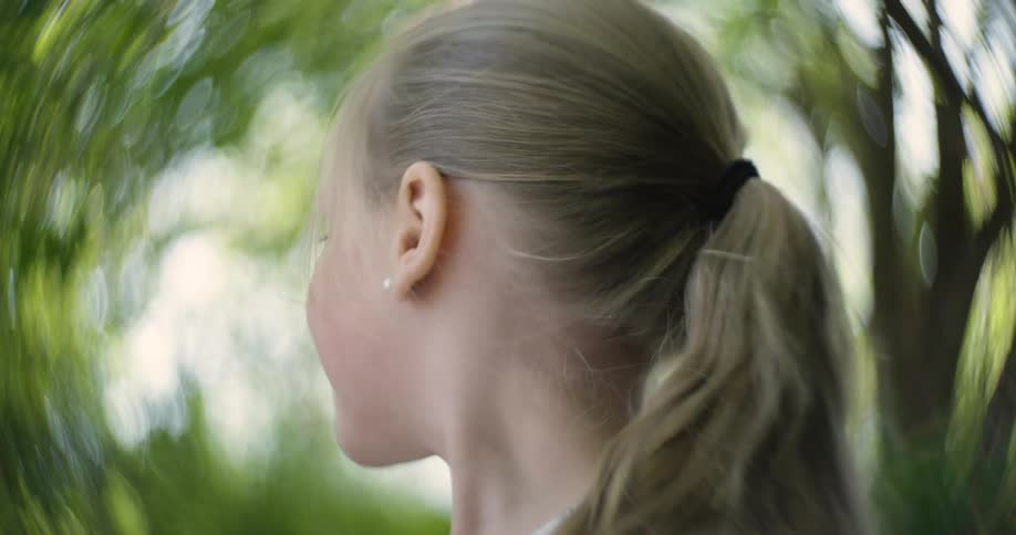 Blonde child looking away with a blurred background of green foliage